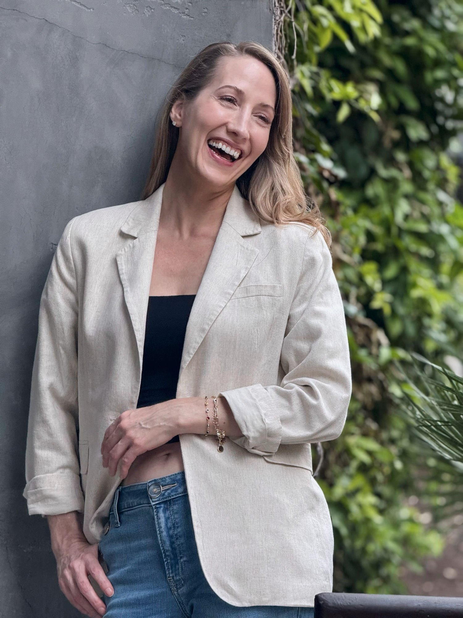 Erin Warner laughing, wearing a linen blazer beside greenery