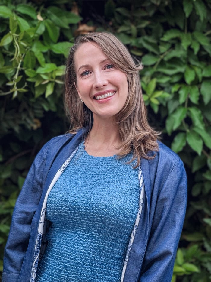 Erin Warner smiling, standing in front of a wall of green foliage